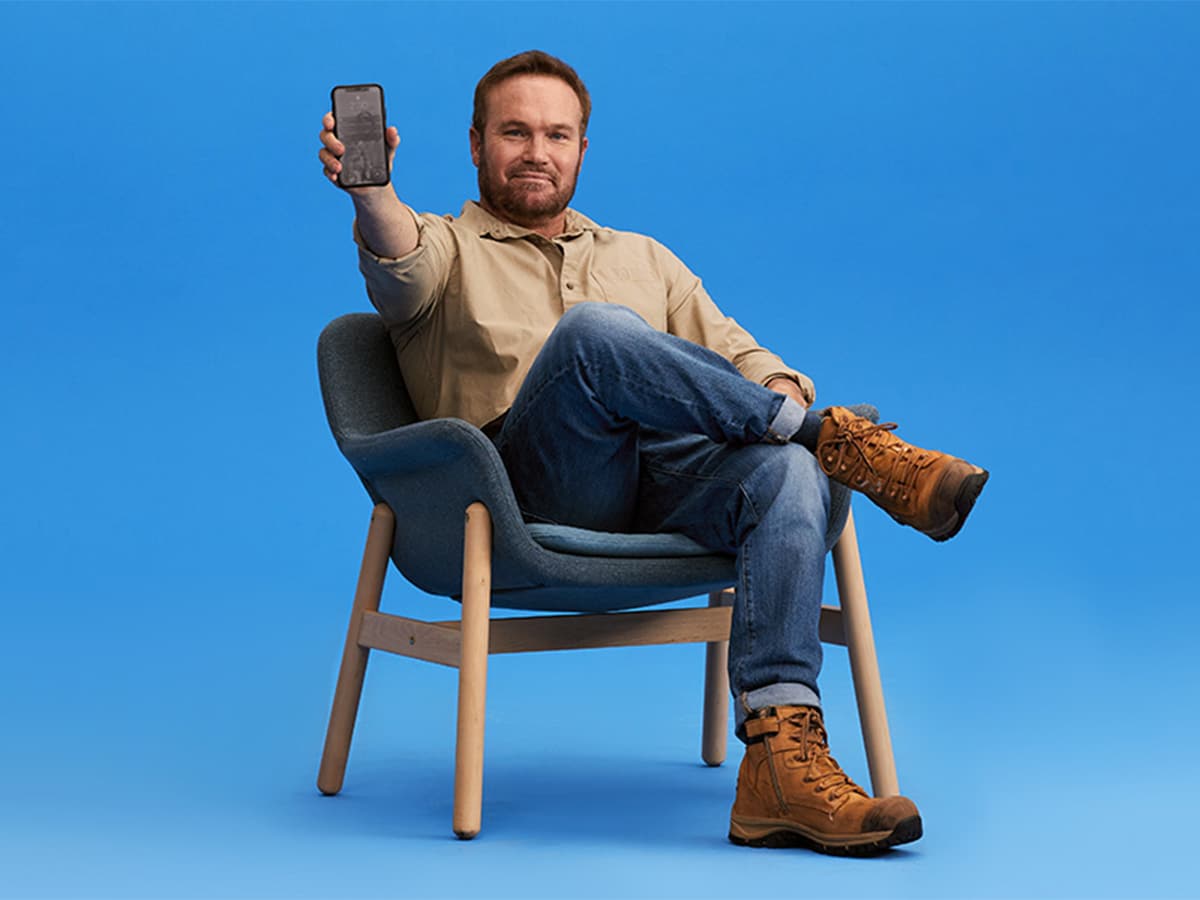 Man sitting on a chair showing his phone screen with blue background