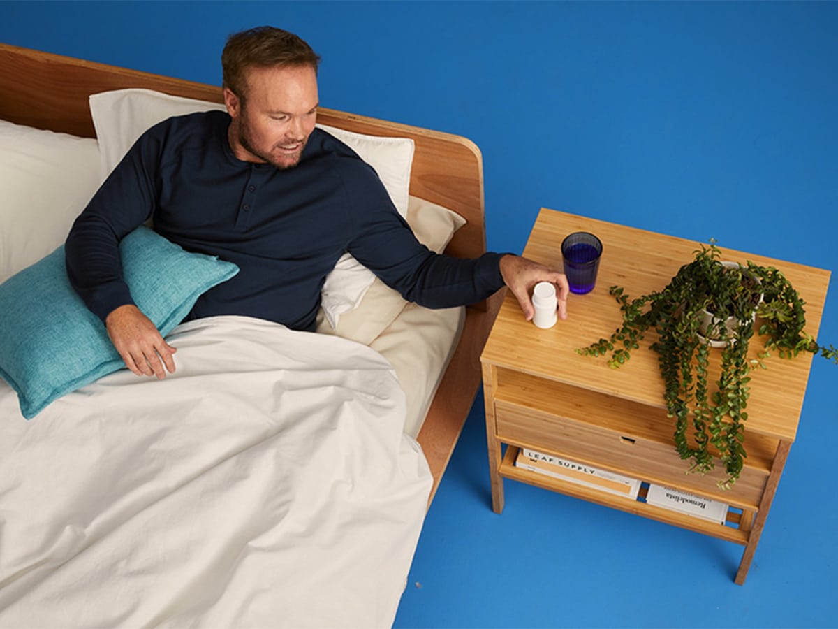 Man in his bed placing his meds on his nightstand with blue background