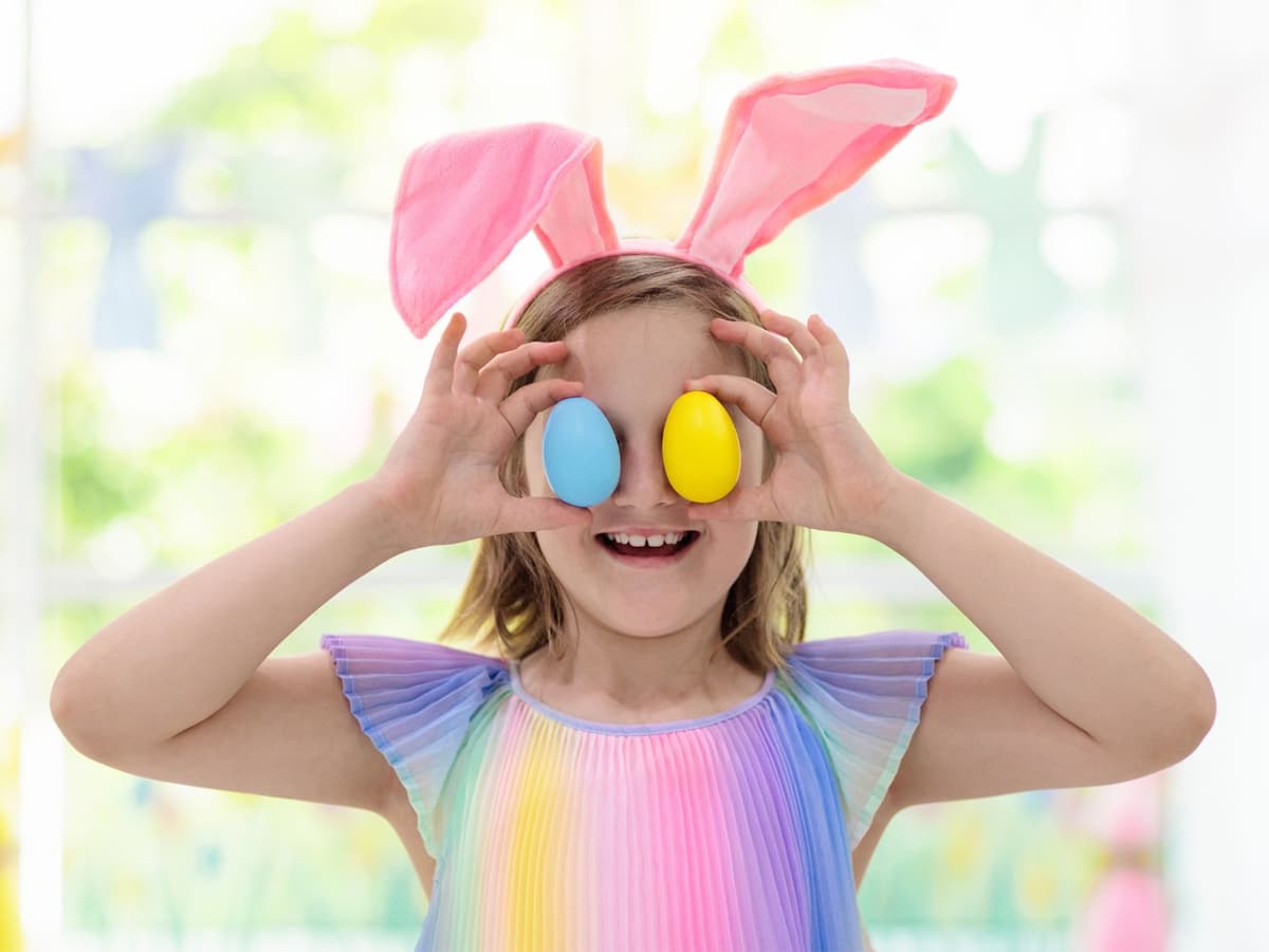 Little girl in an easter bunny costume holding two easter eggs close to her eyes