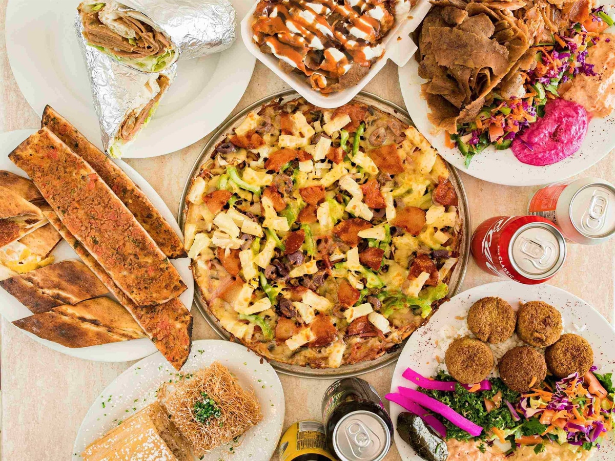 Overhead shot of kebab, pizza, and other food set on a table