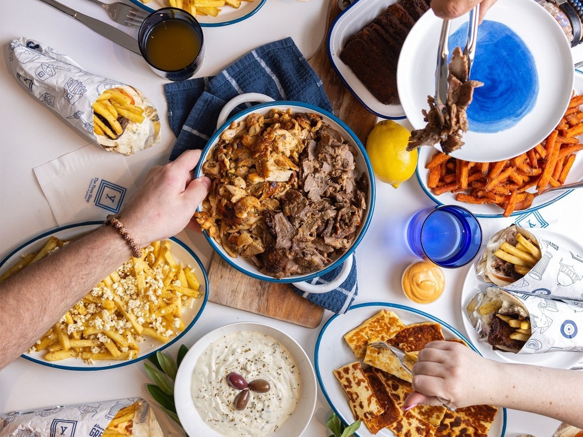 Overhead shot of hands grabbing all kinds of food set on a white table