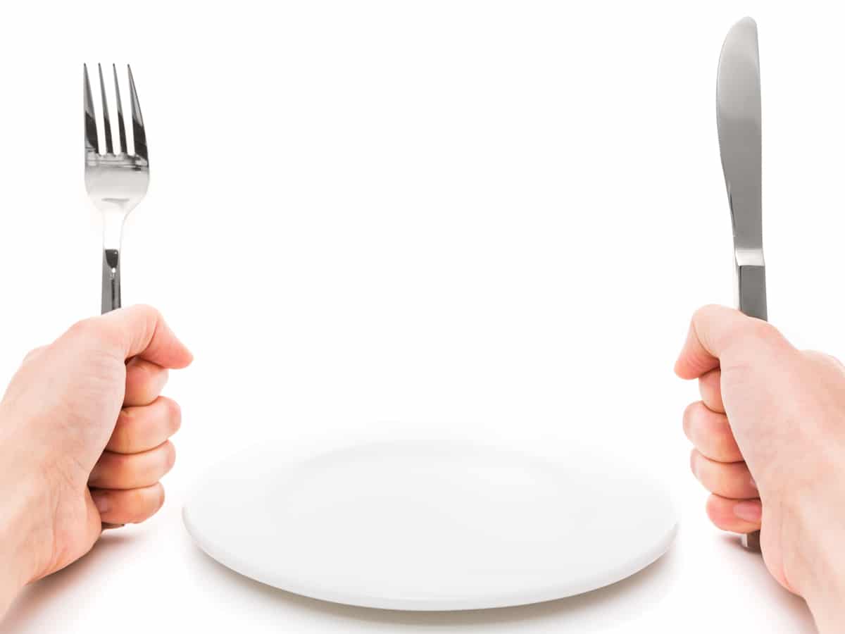 Female hands with cutlery and empty plate on white background
