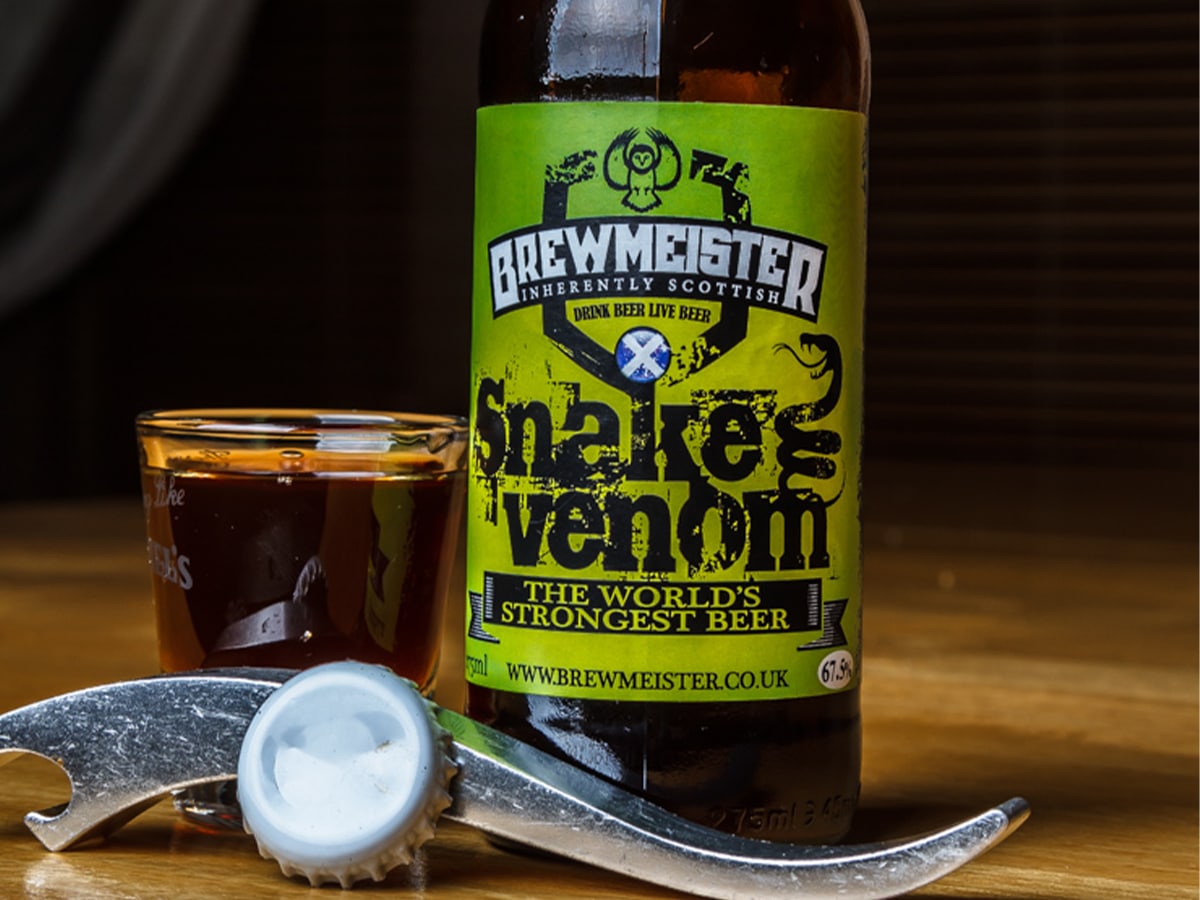 A glass and bottle of Snake Venom beer with a bottle opener set on a wooden table