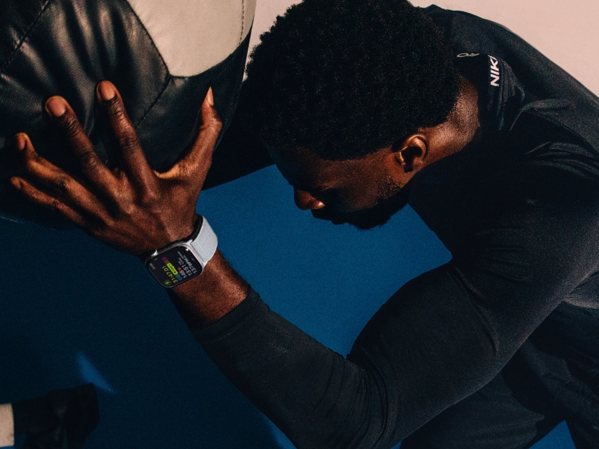 Man wearing a Nike smartwatch while exercising with a medicine ball in a dimly lit gym.