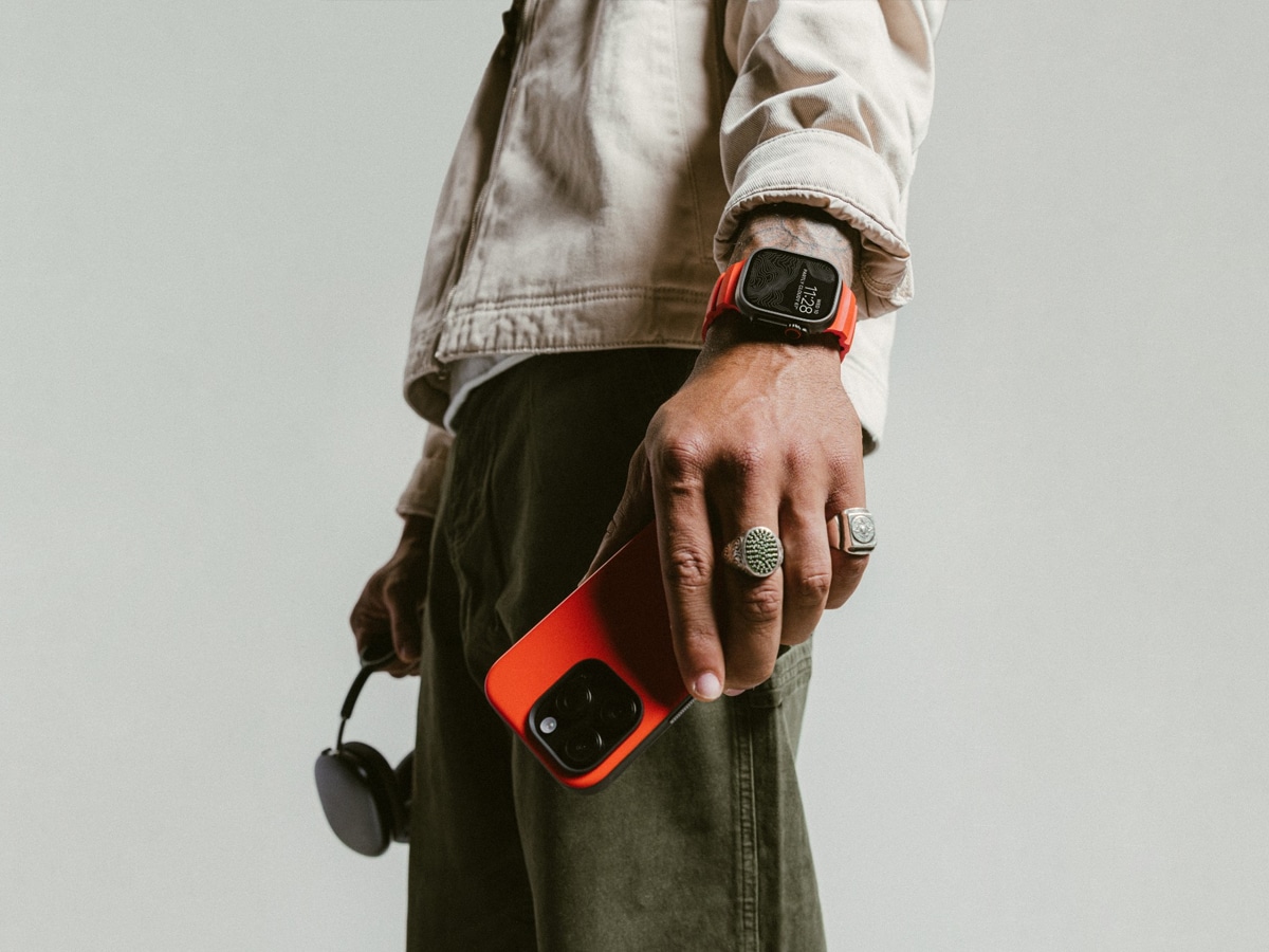 Person wearing a red Apple Watch band holding a red phone, with sunglasses in the other hand.