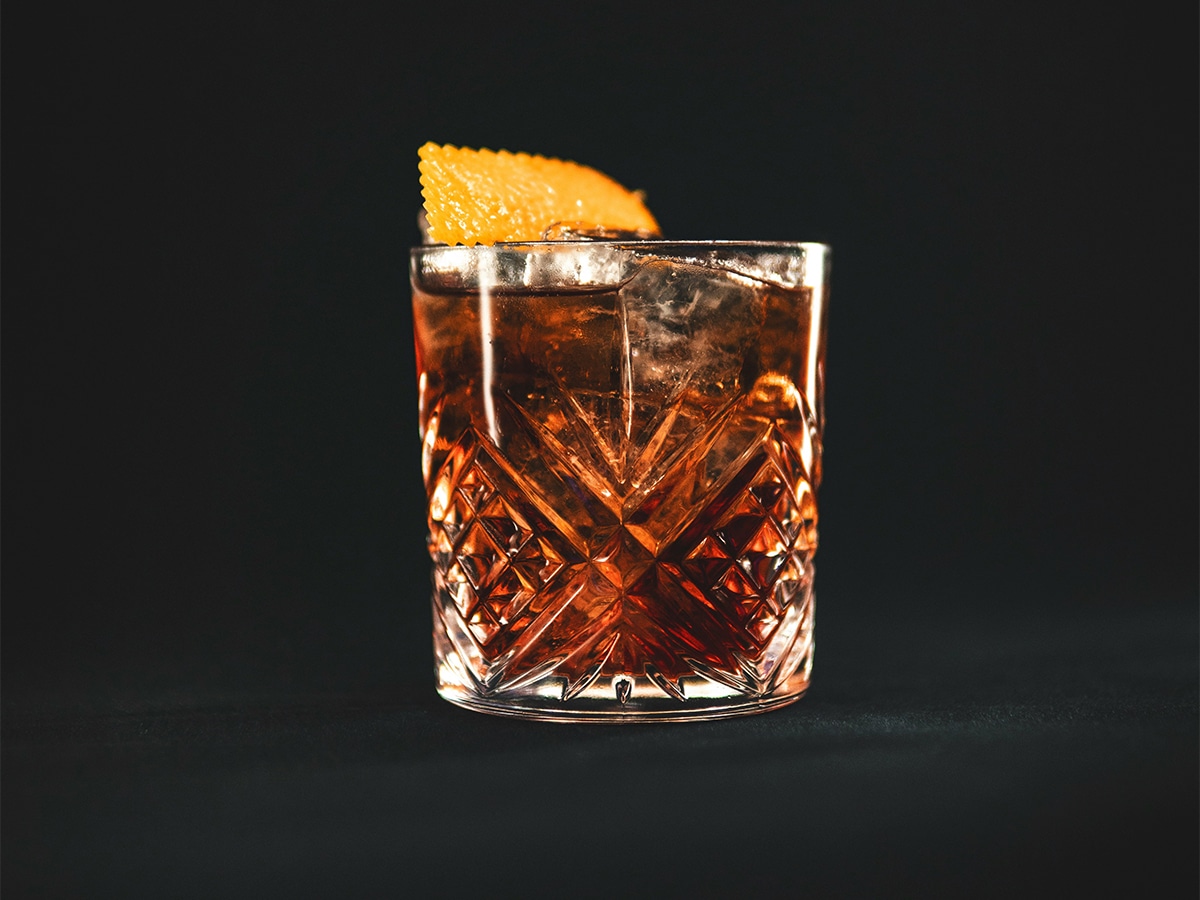 Negroni cocktail in a crystal glass with an orange peel garnish against a dark background.