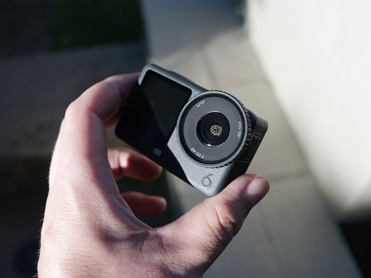 DJI Action 6 camera held in hand, showing lens and screen in outdoor lighting.