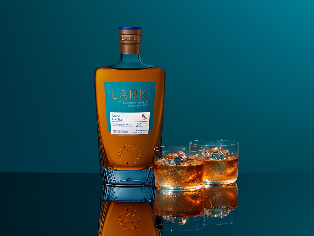Lark Distillery bottle and two glasses of whisky on a reflective blue surface.
