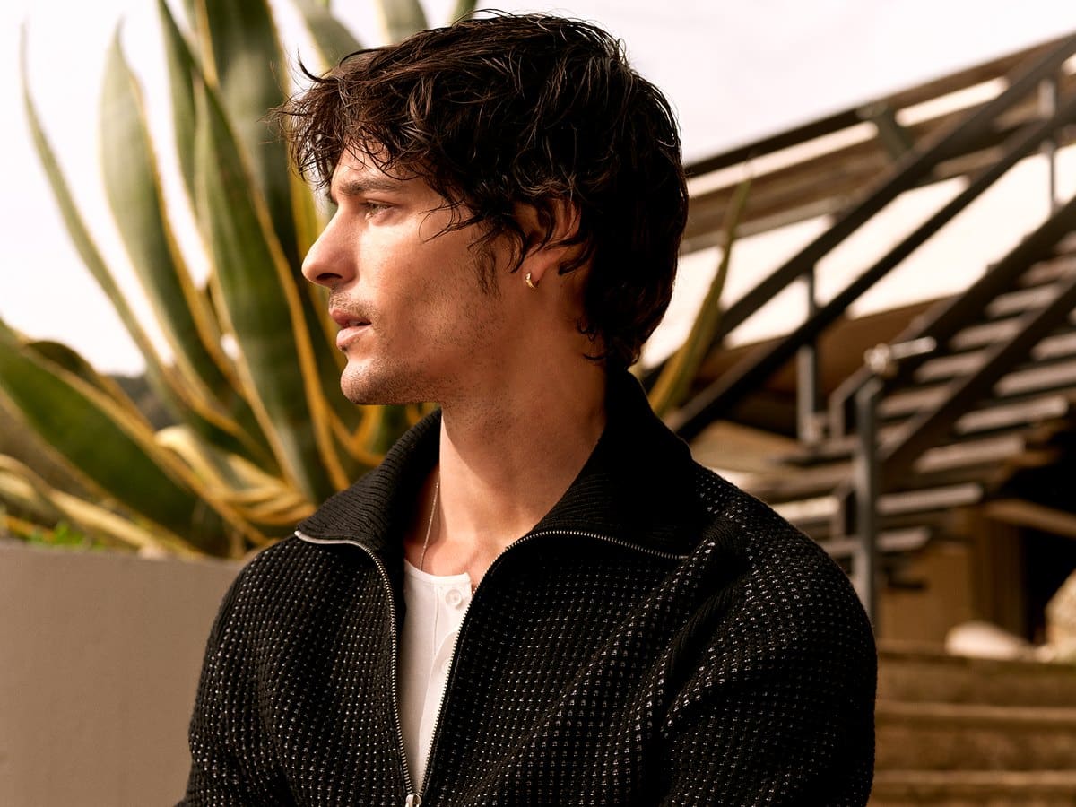 Male model in a black Calibre zip-knit standing by a modernist house