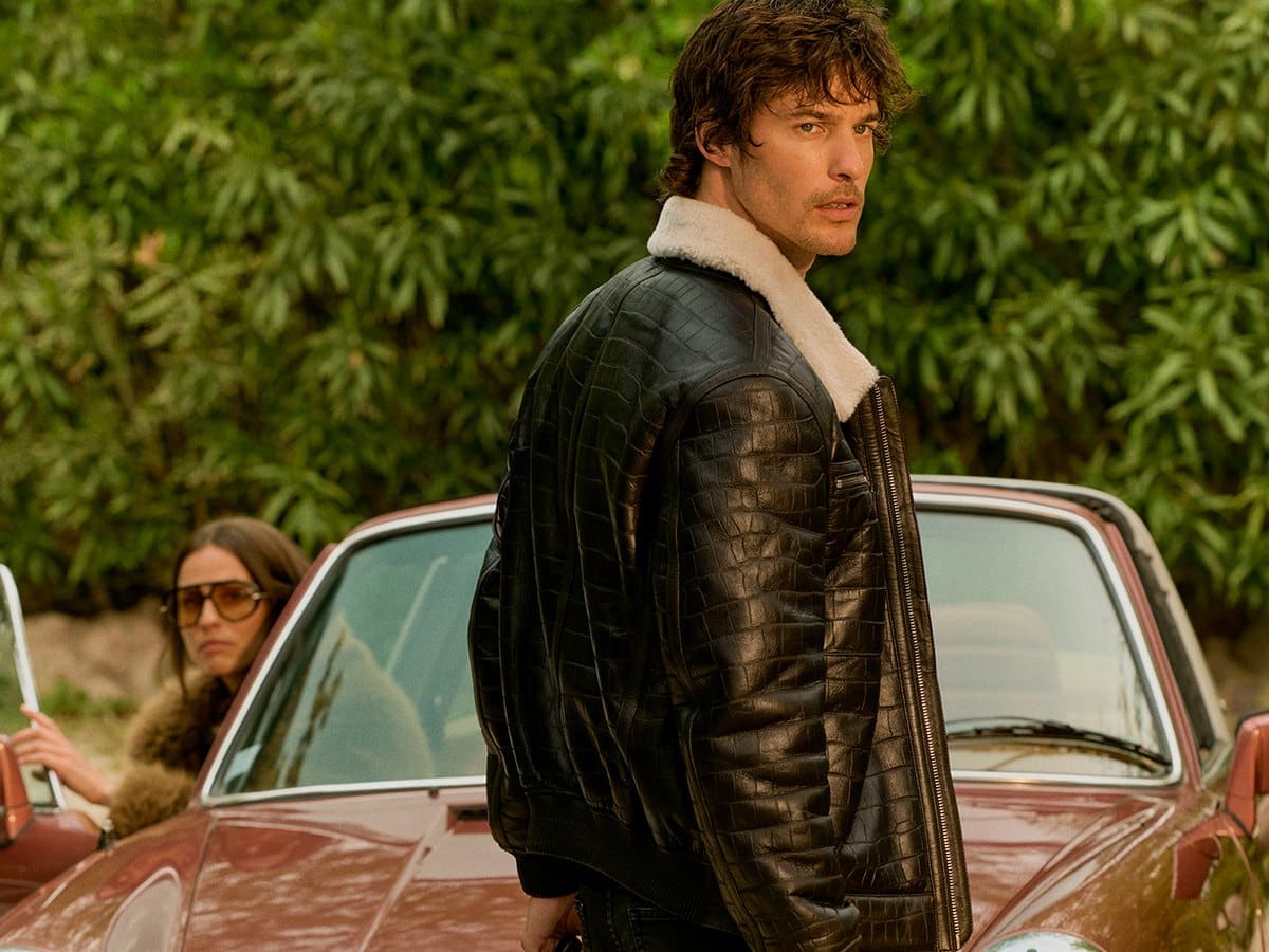 Model in a shearling-collar leather jacket beside a vintage Porsche