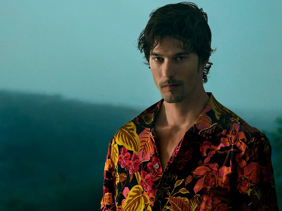 Model wearing the Calibre Tropic Noir rust camp-collar shirt against a mountain backdrop