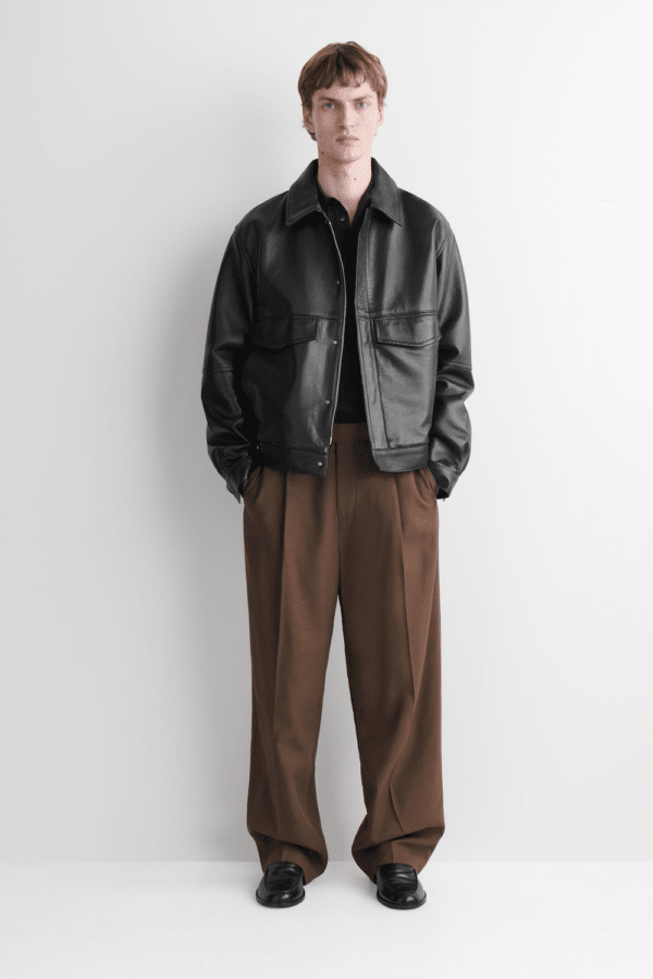 Model styling a COS black leather blouson jacket as a modern corporate blazer alternative for men.