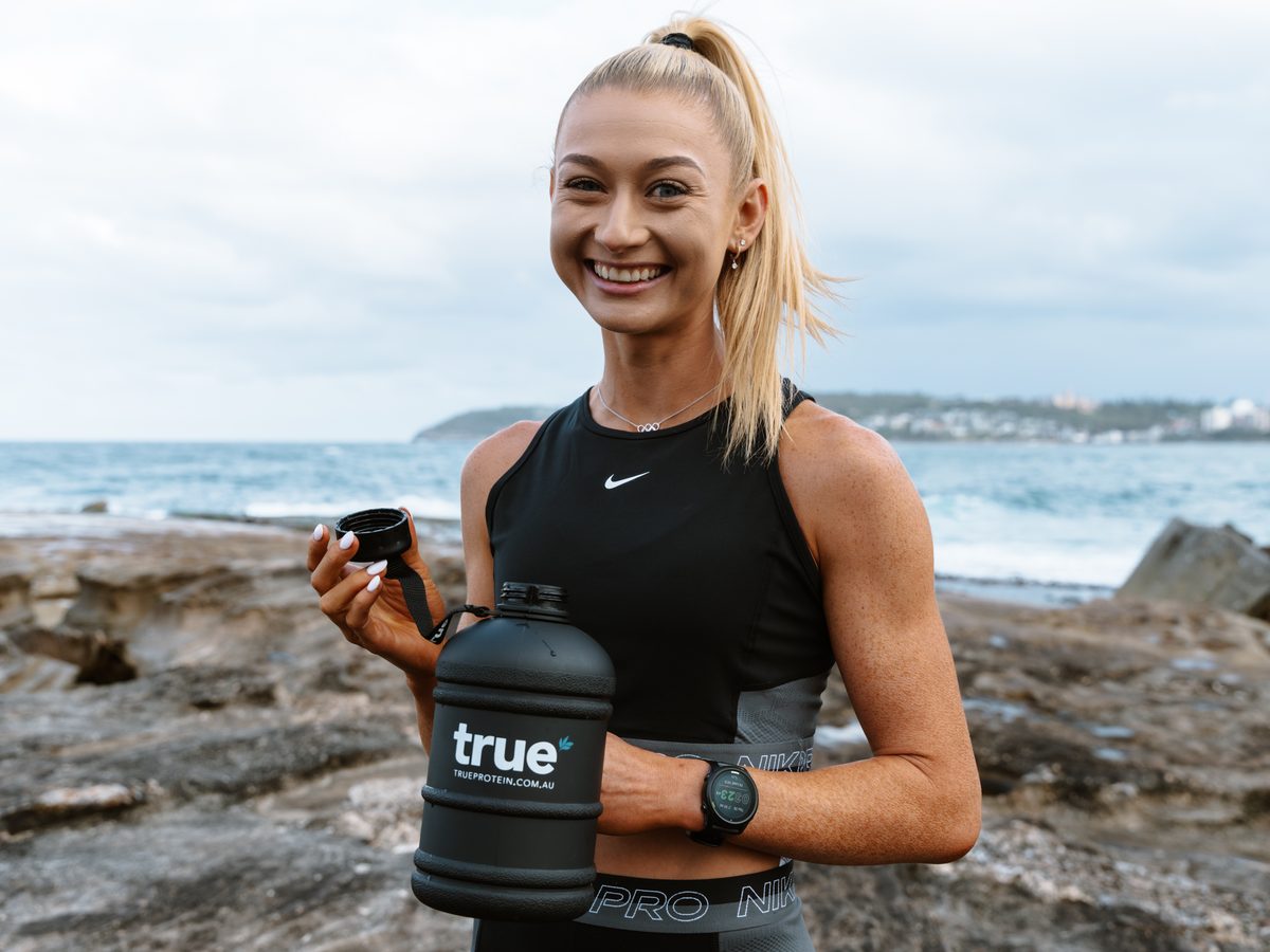 Olympic middle-distance runner Jess Hull smiling and holding a black True Protein water jug on a Sydney headland