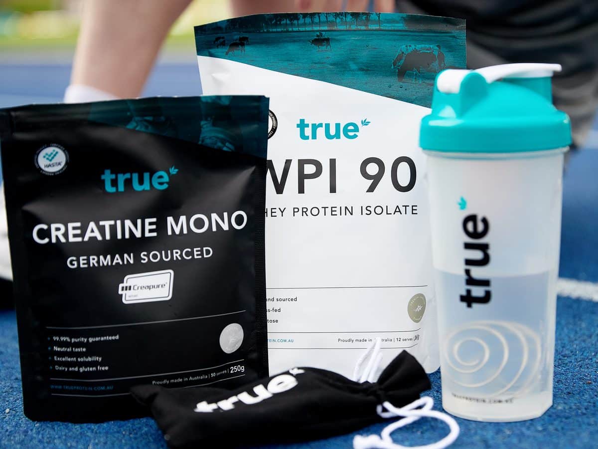 True Protein German-sourced Creatine Mono pouch, WPI 90 whey protein isolate and branded shaker on an athletics track