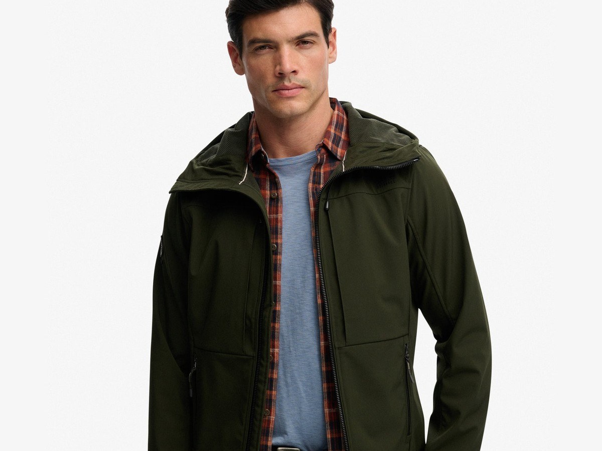 Man wearing the olive green hooded Superdry softshell trekker jacket over a check shirt