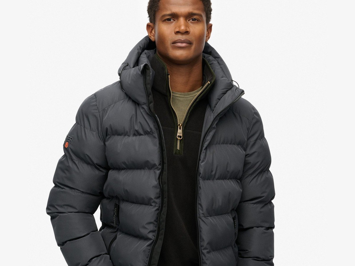 Man wearing the black hooded Superdry sports puffer jacket zipped over a half-zip layer