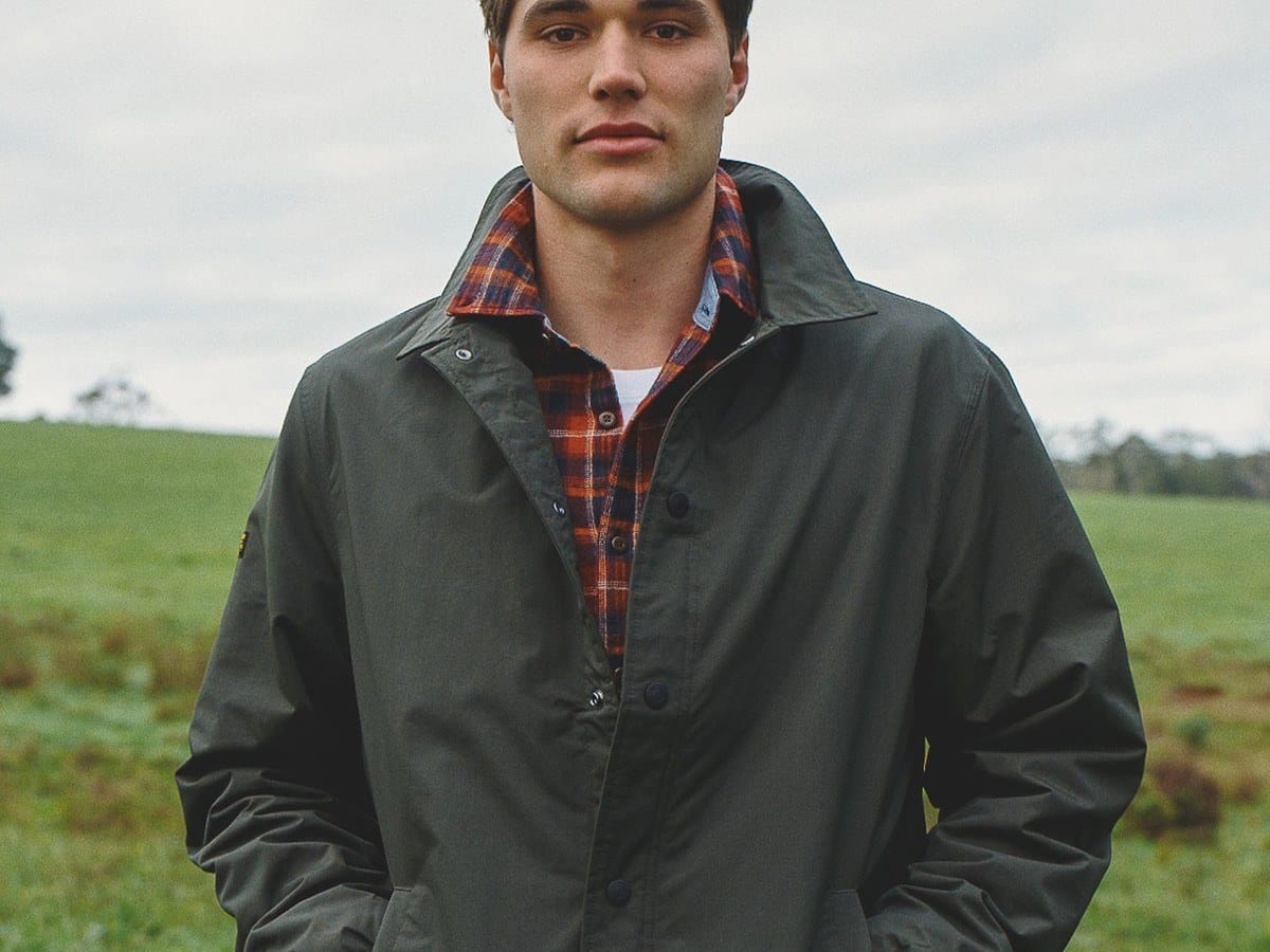 Man wearing the olive Superdry nylon coach jacket over a red check shirt in an open field