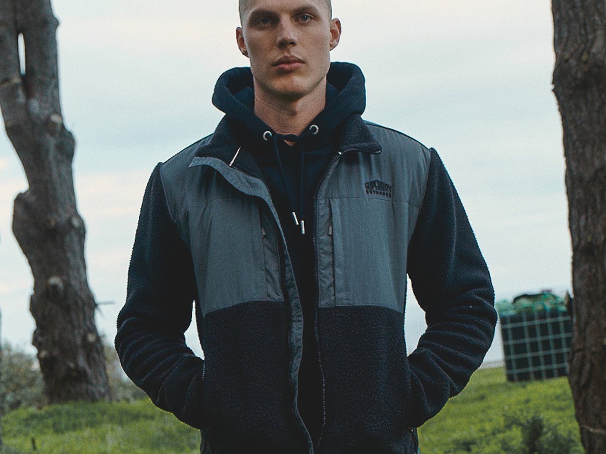 Man wearing the all-black Superdry polar fleece hybrid trekker jacket outdoors under a tree