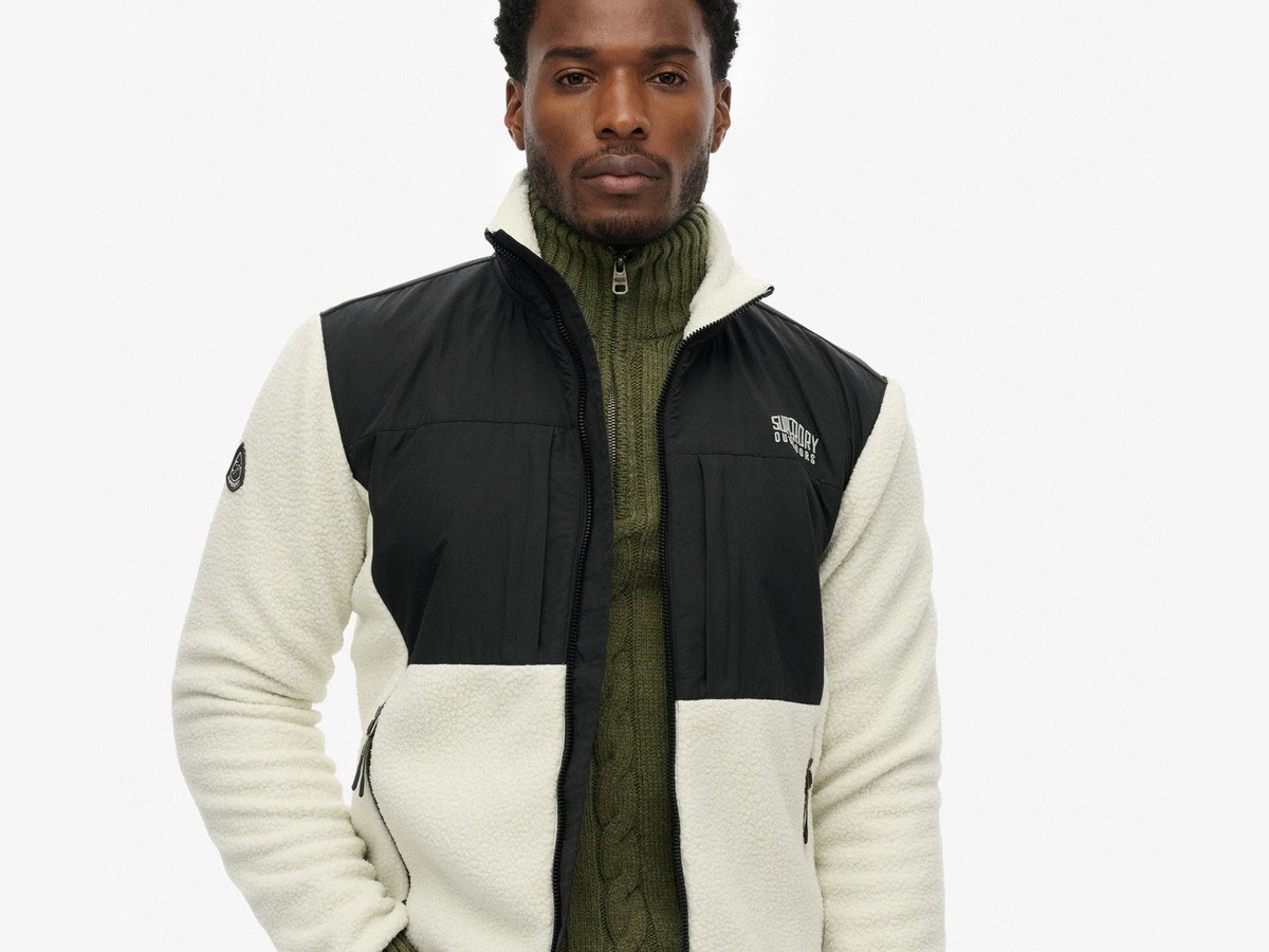 Man wearing the Superdry polar fleece hybrid trekker in cream and black over an olive knit