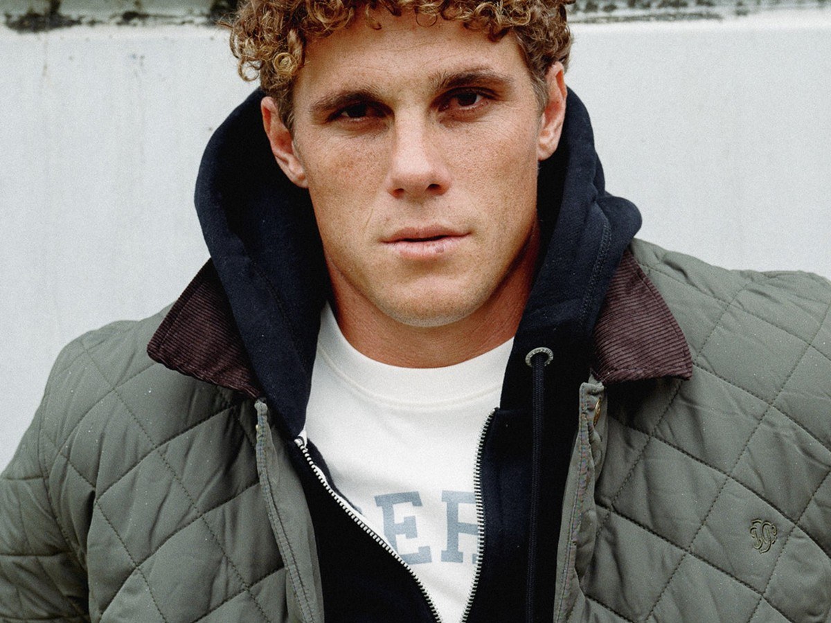 Close-up of a man wearing the quilted Superdry Estate jacket in olive green over a navy hoodie