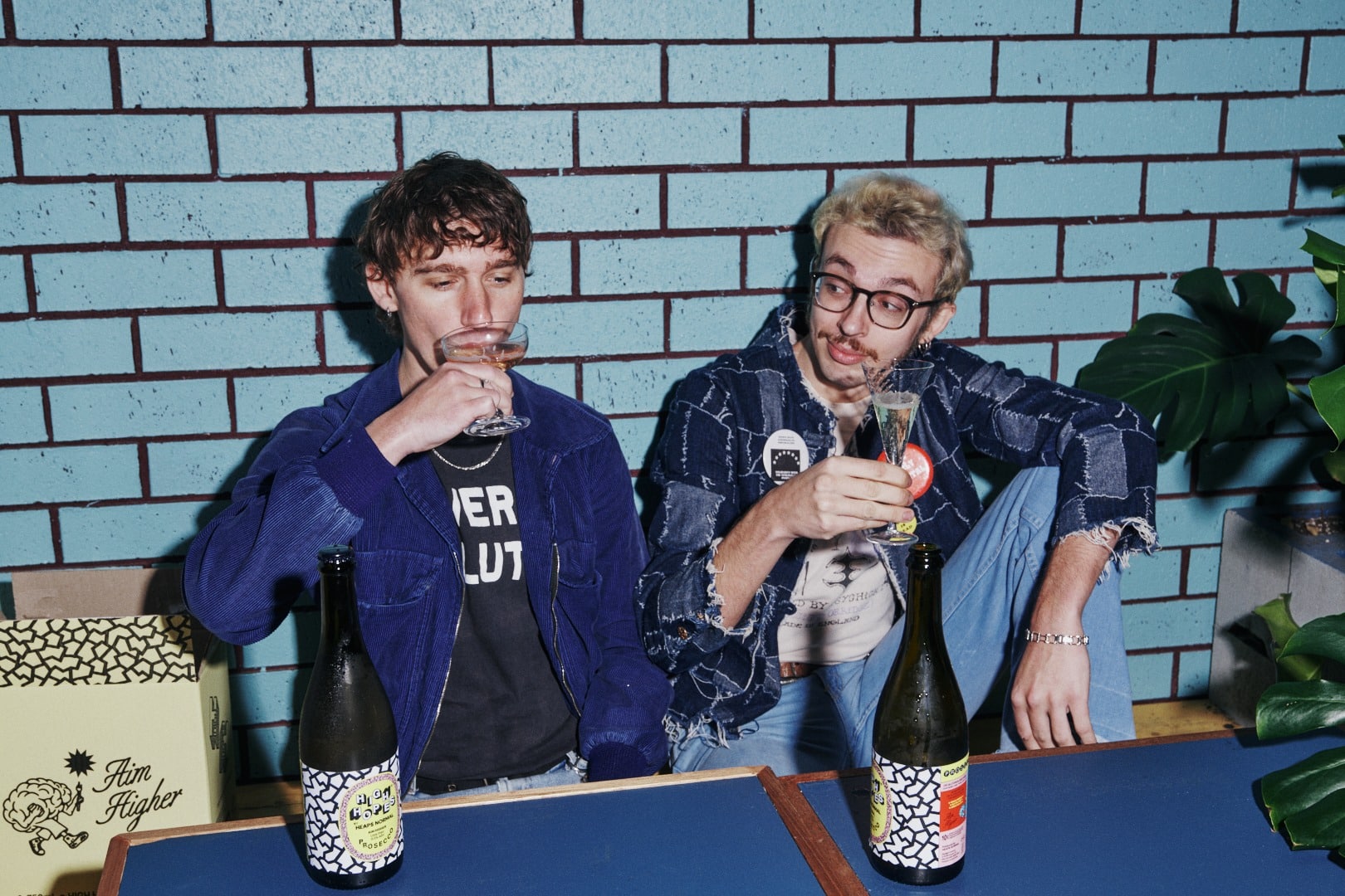 Two friends toasting High Hopes prosecco against a blue-brick wall
