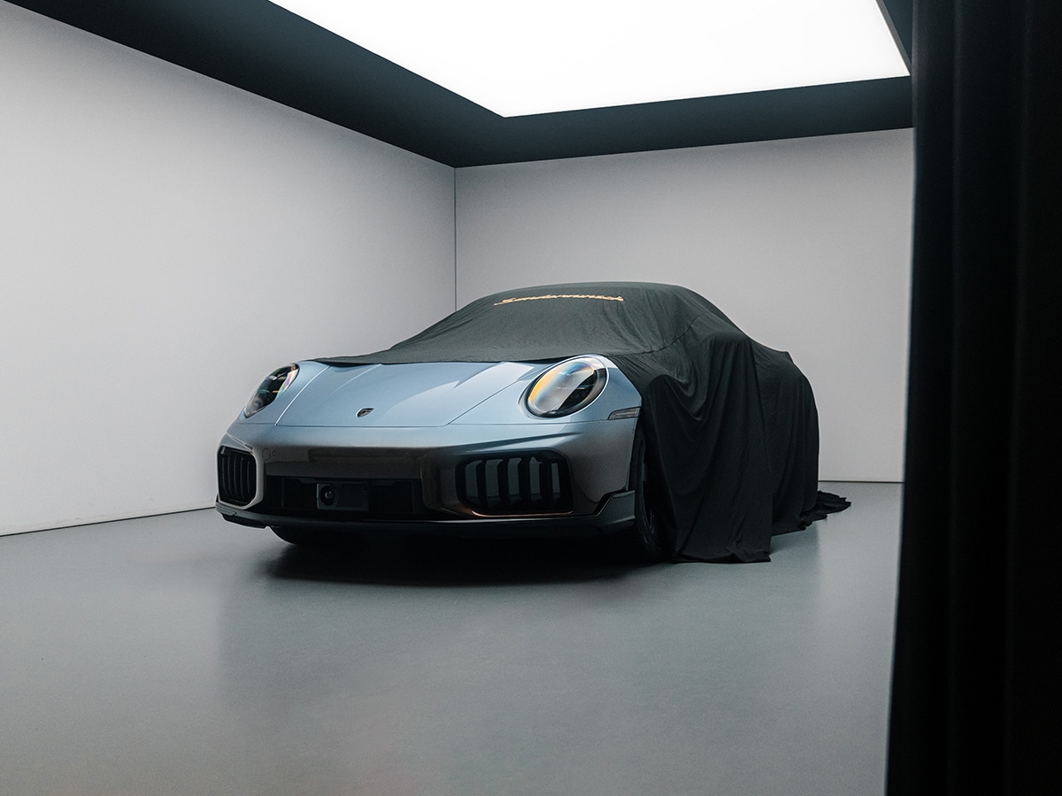 A Porsche 911 Turbo S covered with a black cloth in a gallery