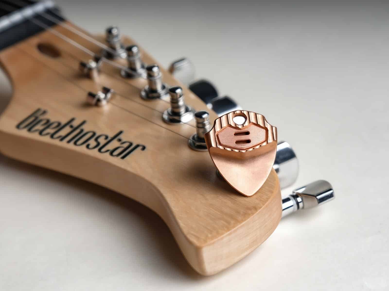 A copper EchoTi pick held magnetically against a maple electric guitar headstock