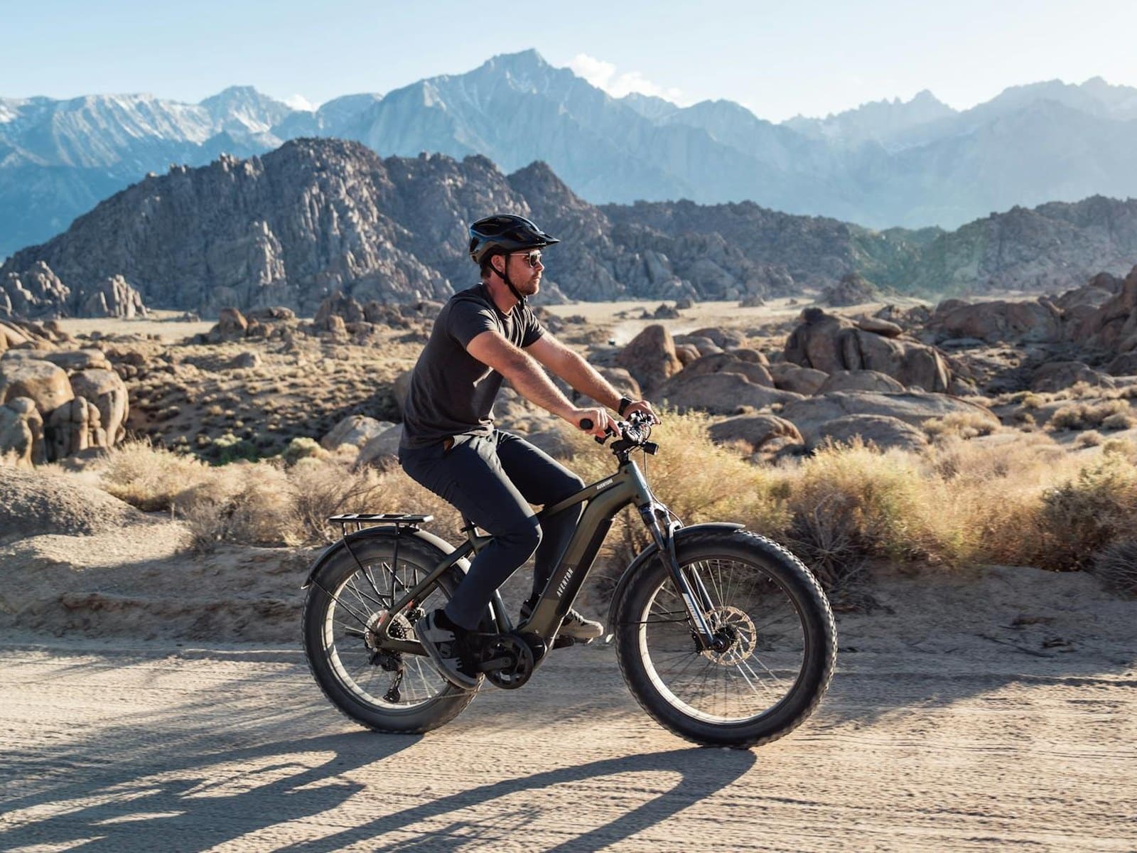 A rider on an Aventon Aventure fat tyre electric bike on a desert trail with mountains behind