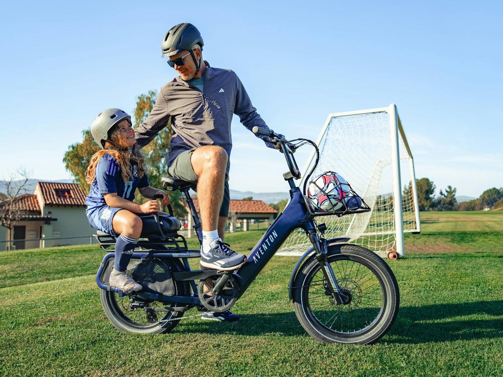 An adult and a child on an Aventon Abound cargo electric bike fitted with a rear passenger seat