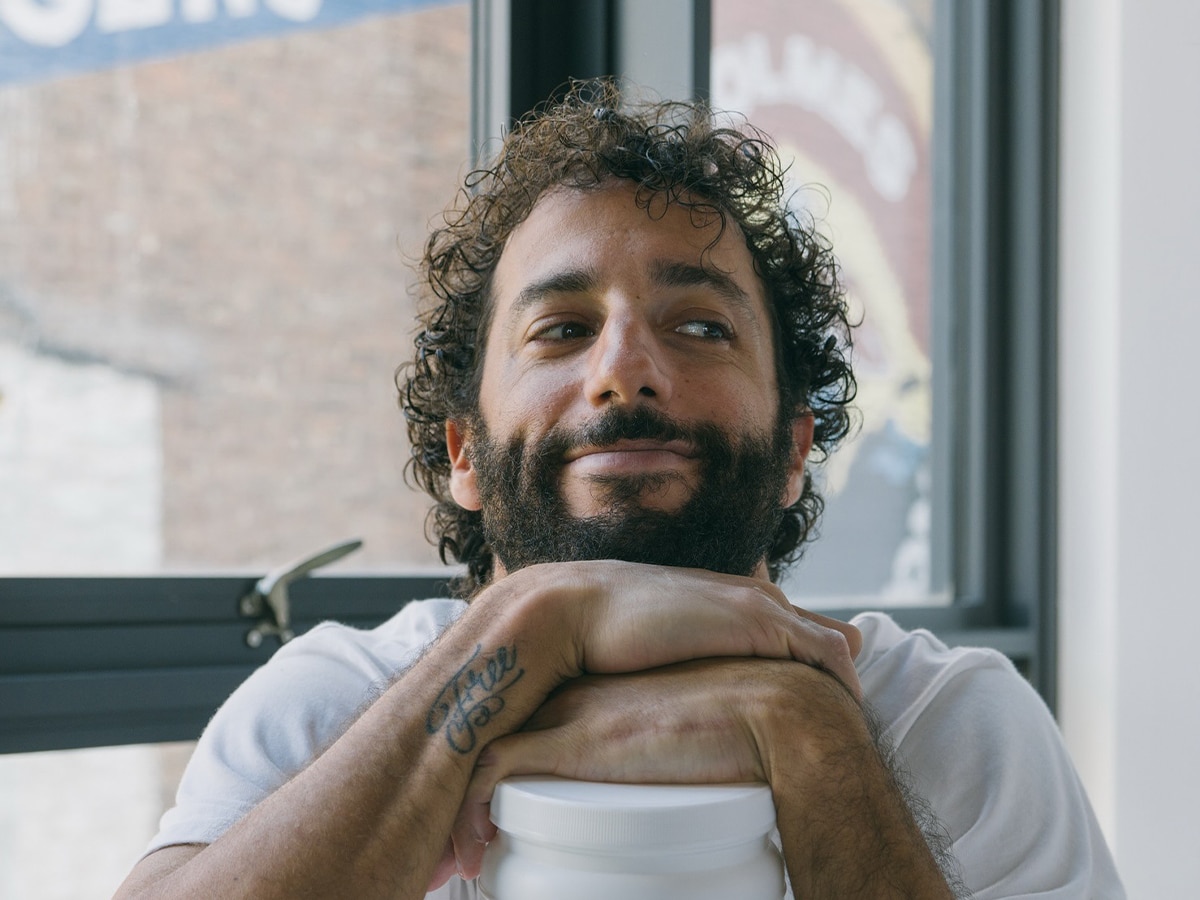 Close-up portrait of Daniel Ricciardo with curly hair and a full beard, resting his chin on his hands while looking off-camera.