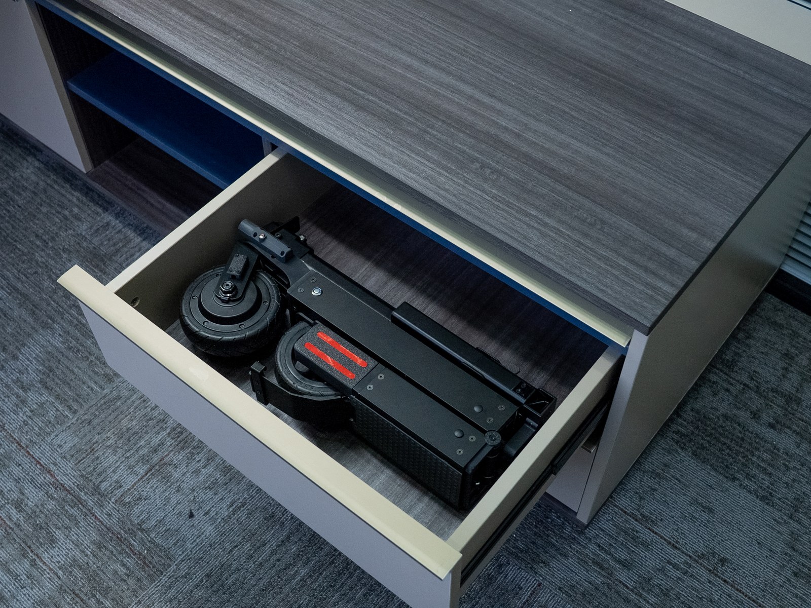 Folded Blizwheel F0.5 scooter lying inside an open office desk drawer