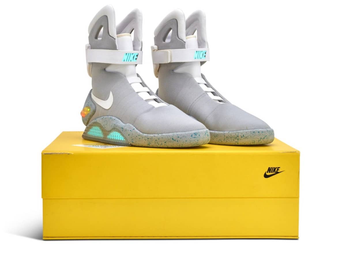 A pair of 2011 Nike MAG shoes with illuminated NIKE straps and glowing outsoles resting on the original yellow Nike box
