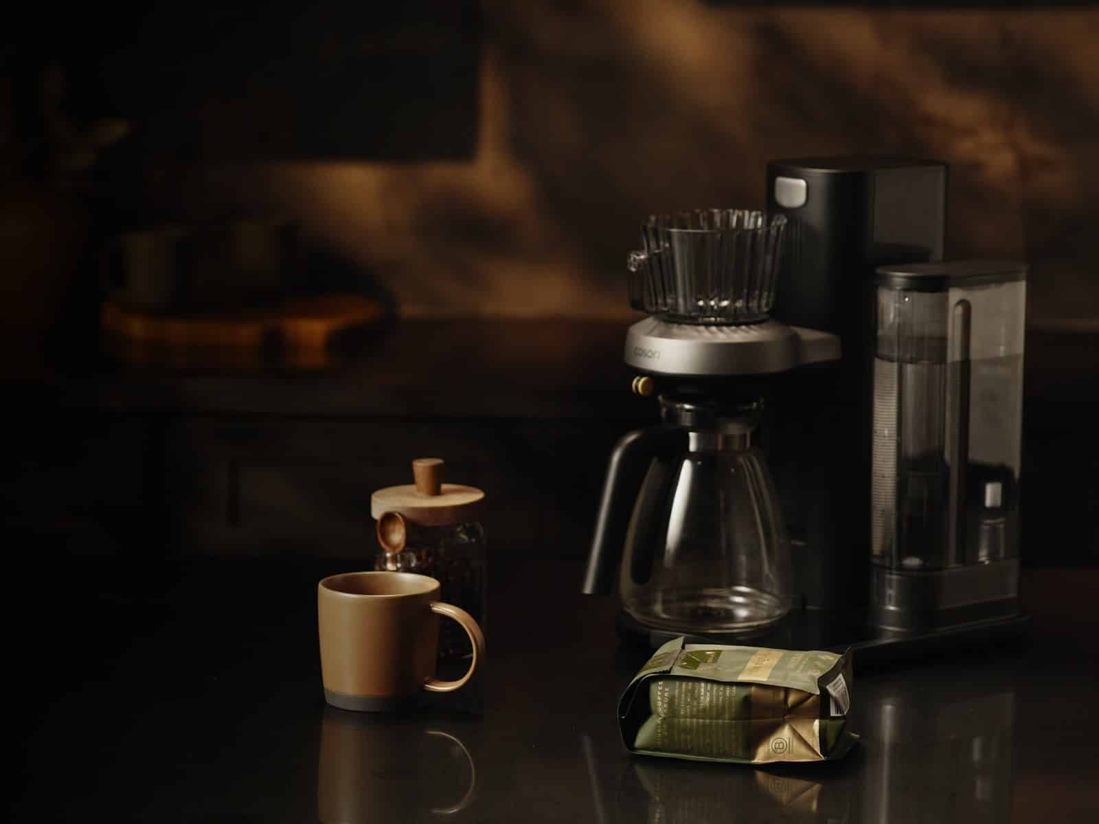 The Cosori JUNI on a dark counter with a mug and a bag of coffee beans