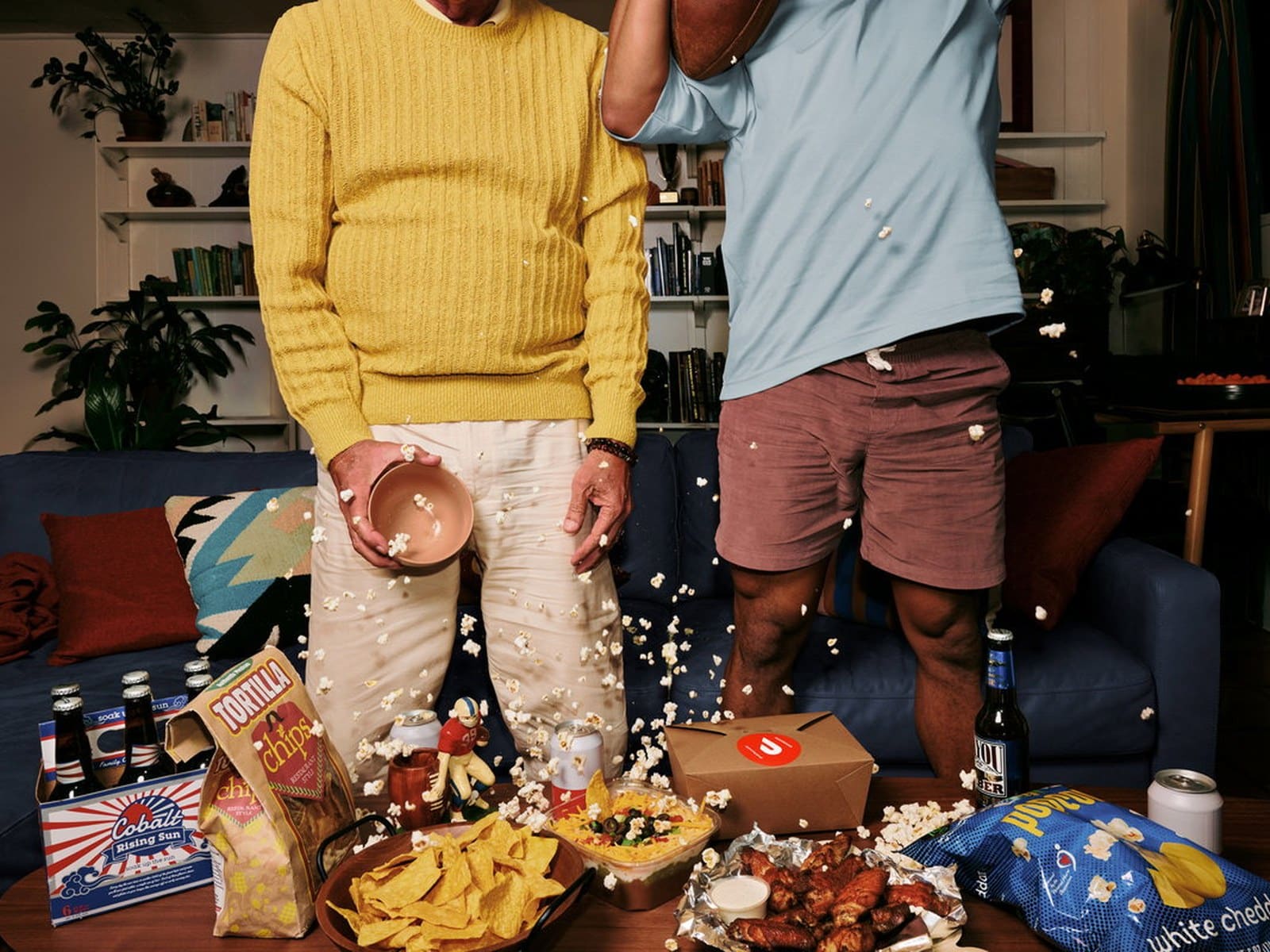Friends hosting a game-day watch party at home with food delivered.