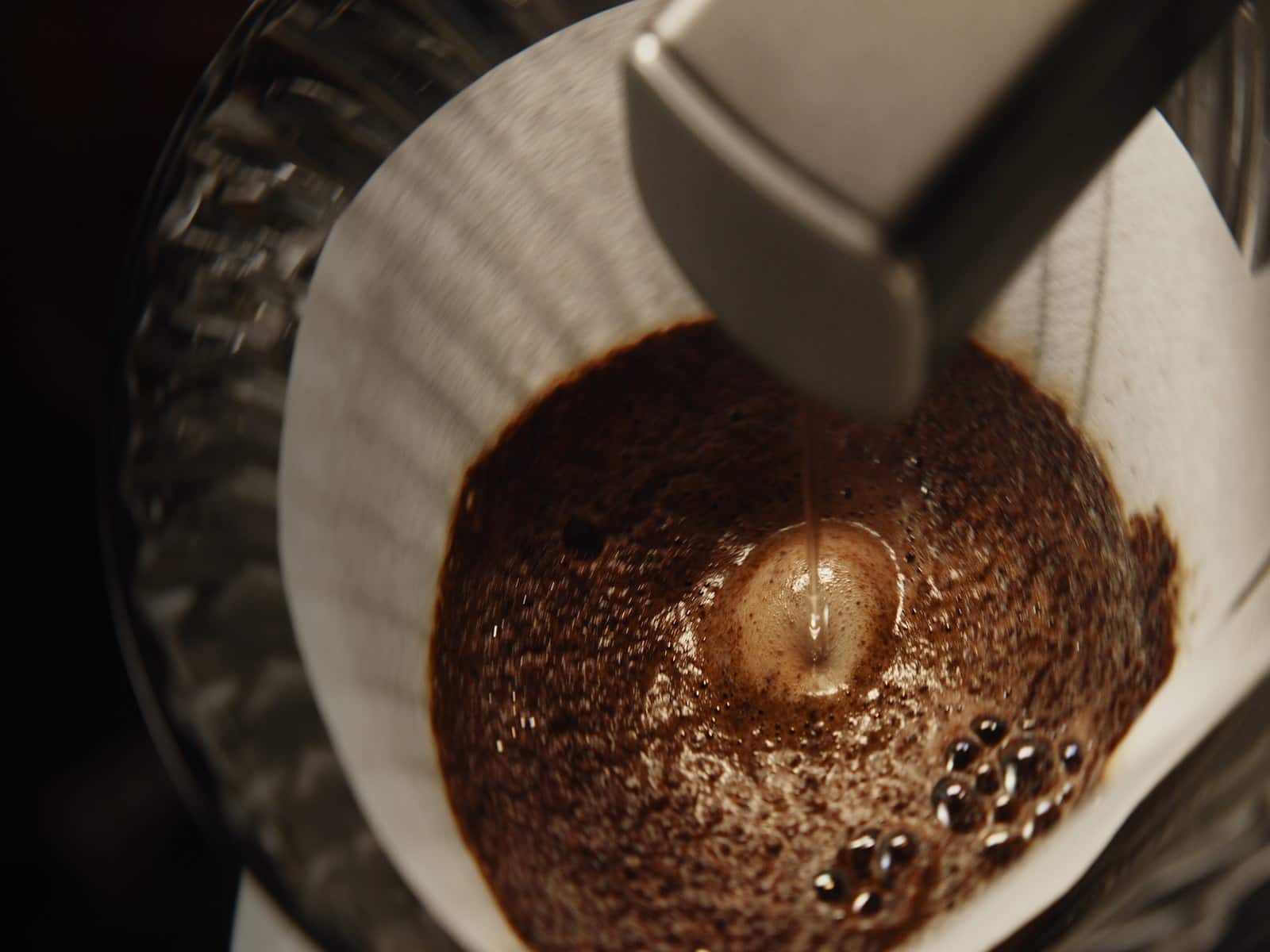 The nozzle pouring a stream of water onto a dark bed of coffee grounds