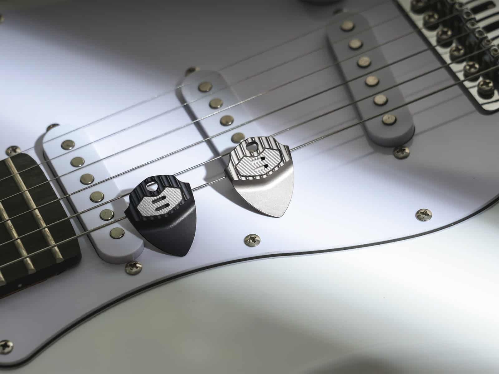 Two EchoTi picks lying on the strings and pickups of a white electric guitar
