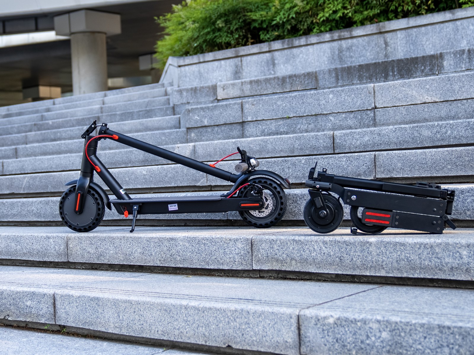 Folded Blizwheel F0.5 on granite steps beside a conventional folded electric commuter scooter, showing the size difference
