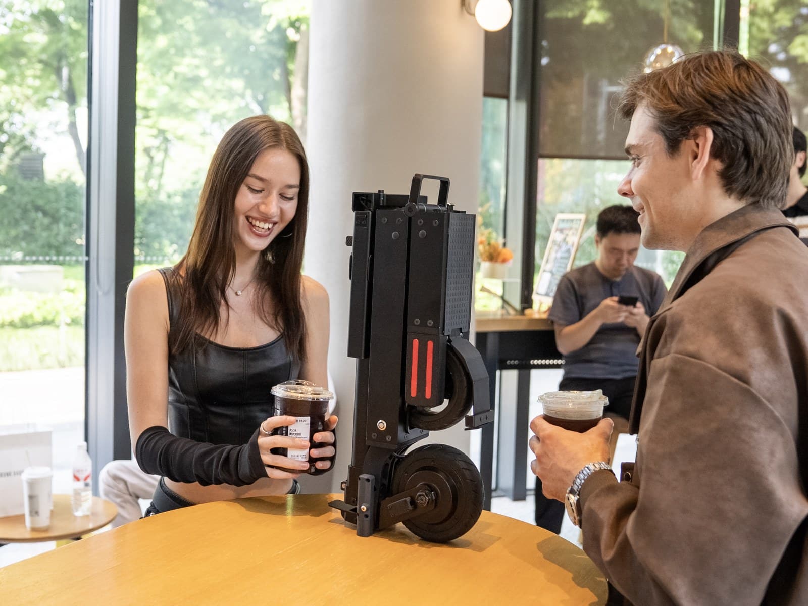 Folded Blizwheel F0.5 electric scooter standing upright on a cafe table between two people holding iced coffees