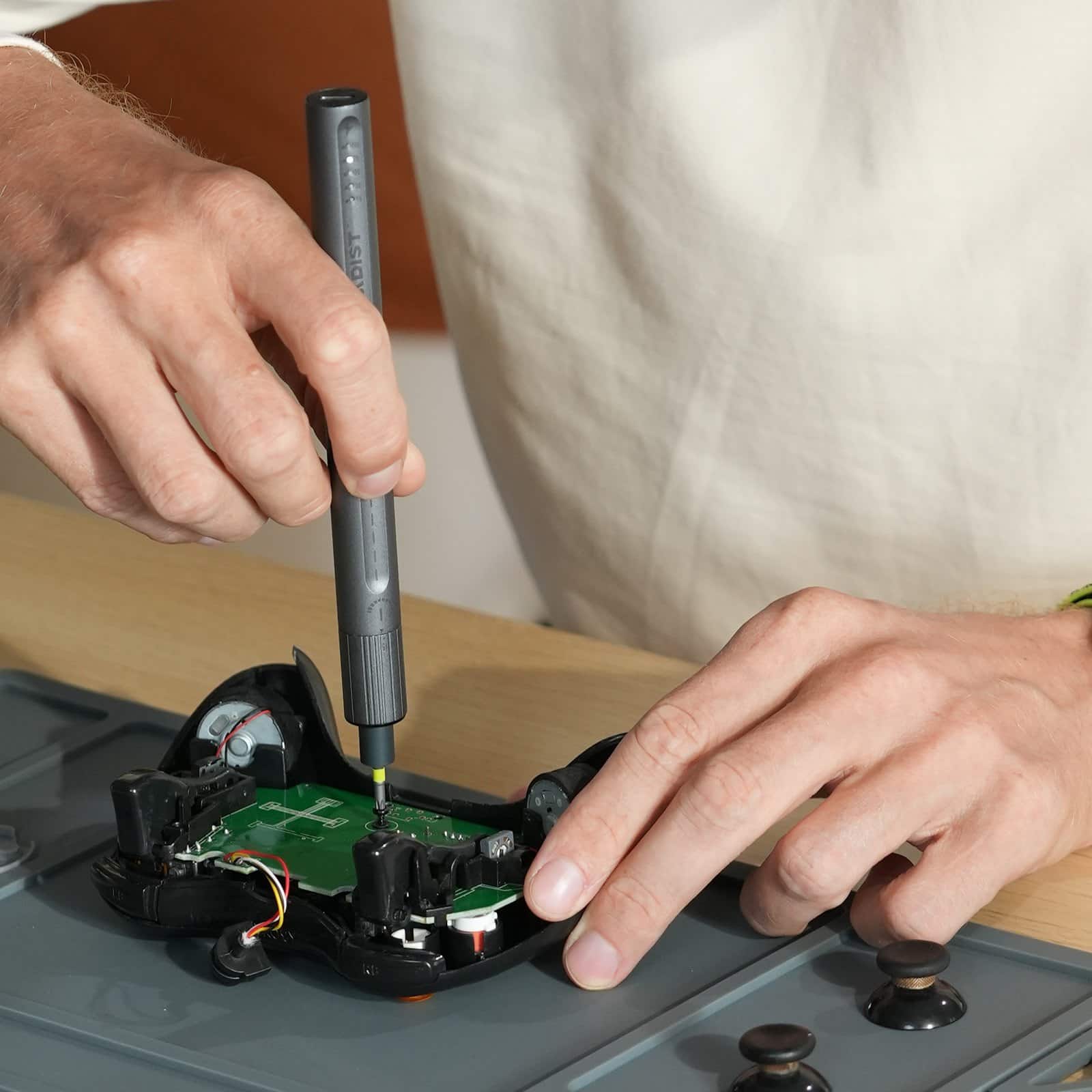 Hands using the Cladist Titan to repair the circuit board inside a games console controller on a work mat
