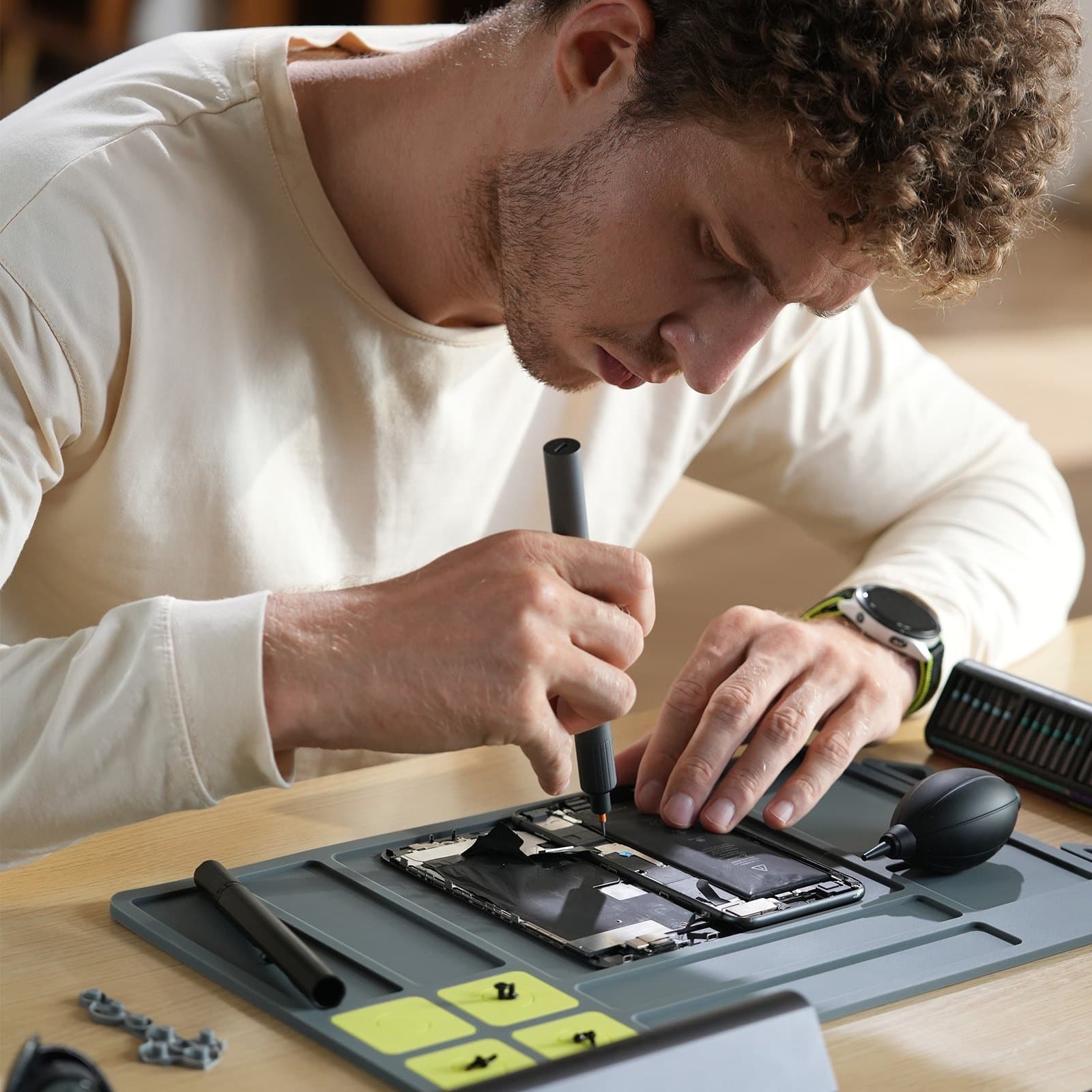 Man using the Cladist Titan electric screwdriver to open a laptop on a repair mat, with the bit case and tools laid out beside him