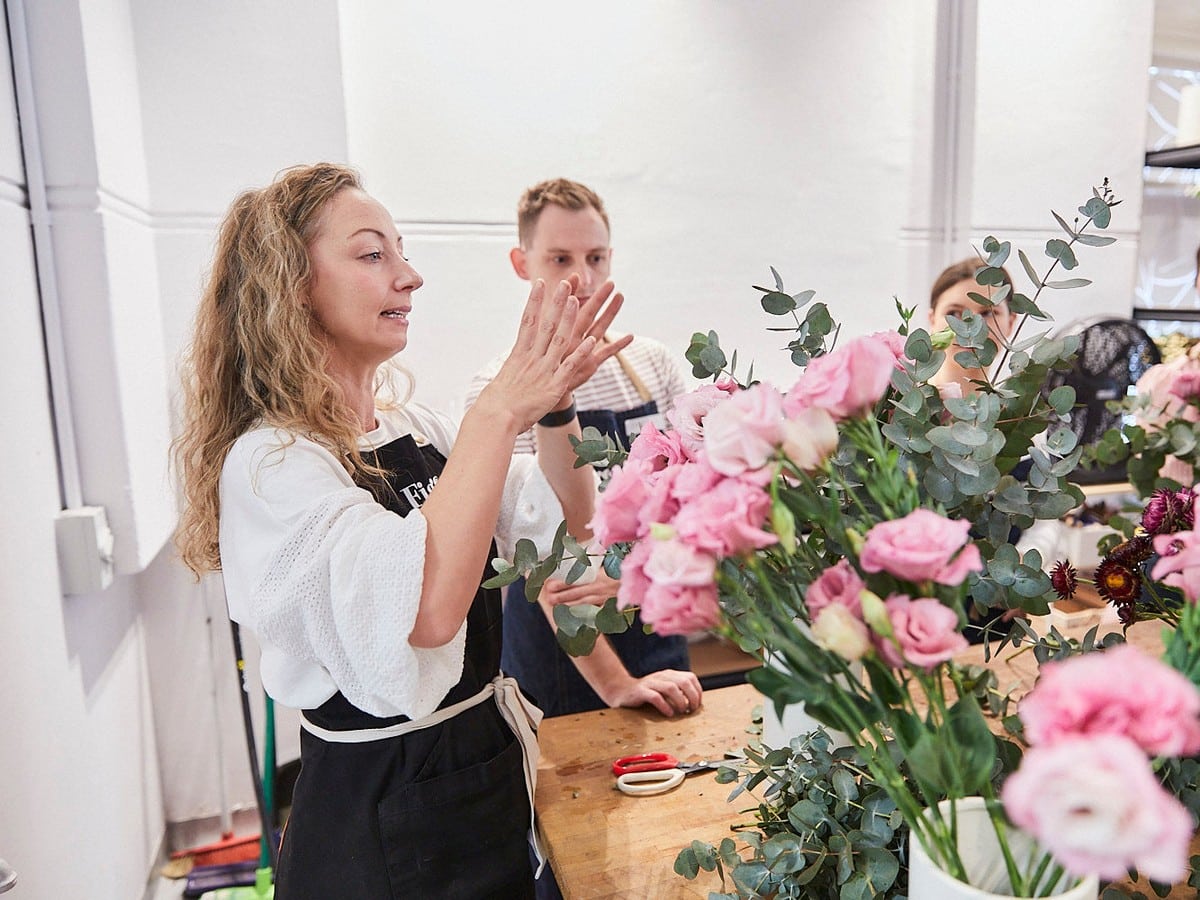 Fig & Bloom florist demonstrating an arrangement to attendees at a studio workbench