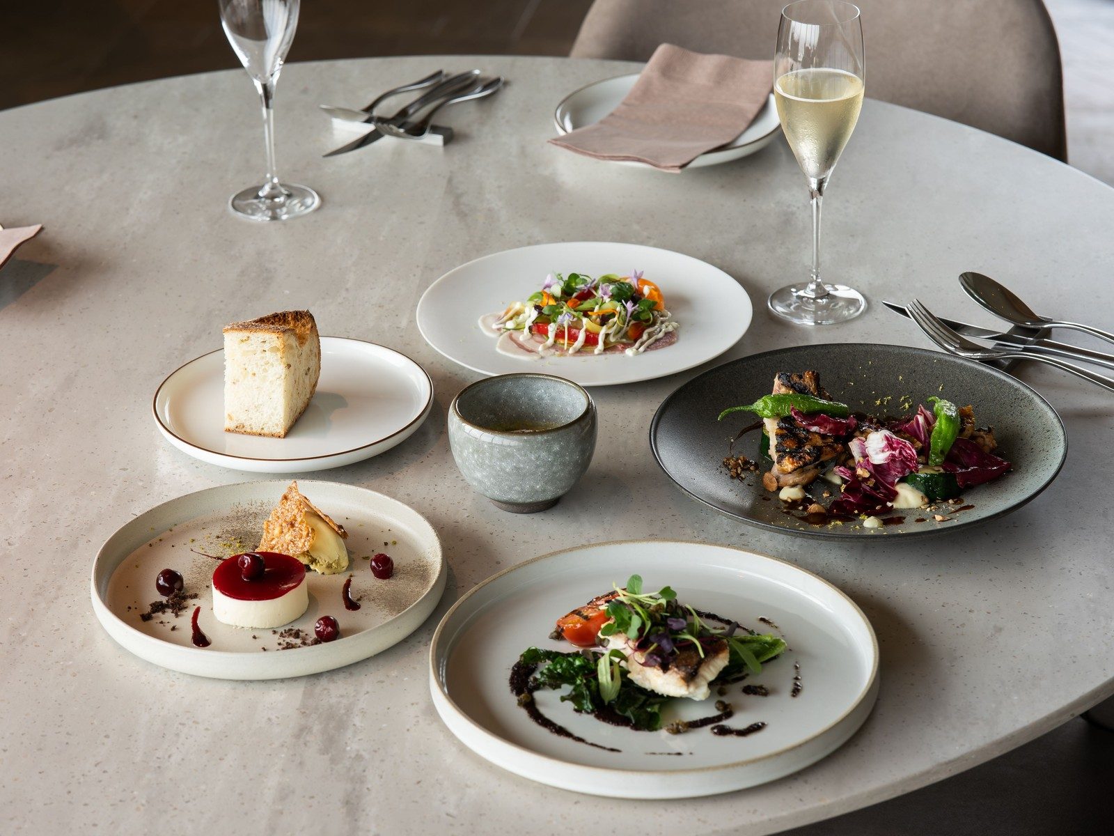 A restaurant table set with several plated fine dining courses and two glasses of wine