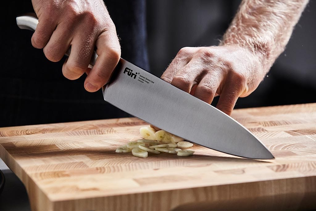 Slicing garlic thinly with a Furi Pro chef's knife on an end-grain board