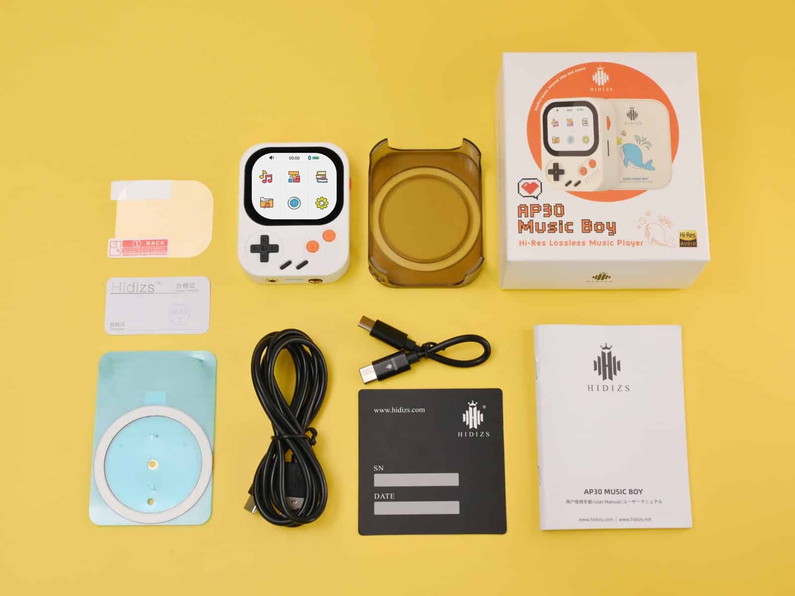 Hidizs AP30 Music Boy unboxed on a yellow background with its retail box, USB-C cable, silicone case, documentation and accessories laid out around it