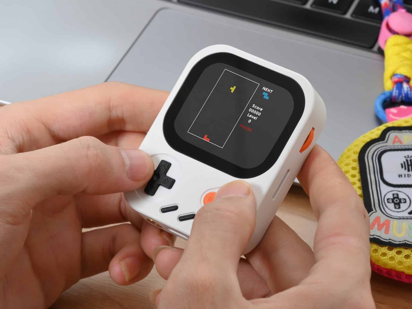 Two hands holding a white Hidizs AP30 Music Boy and pressing the D-pad, with a block-stacking game running on the screen