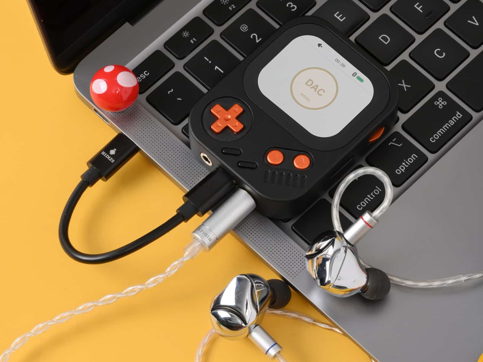 Hidizs AP30 Music Boy plugged into a laptop's USB-C port with in-ear monitors attached, on a yellow desk surface