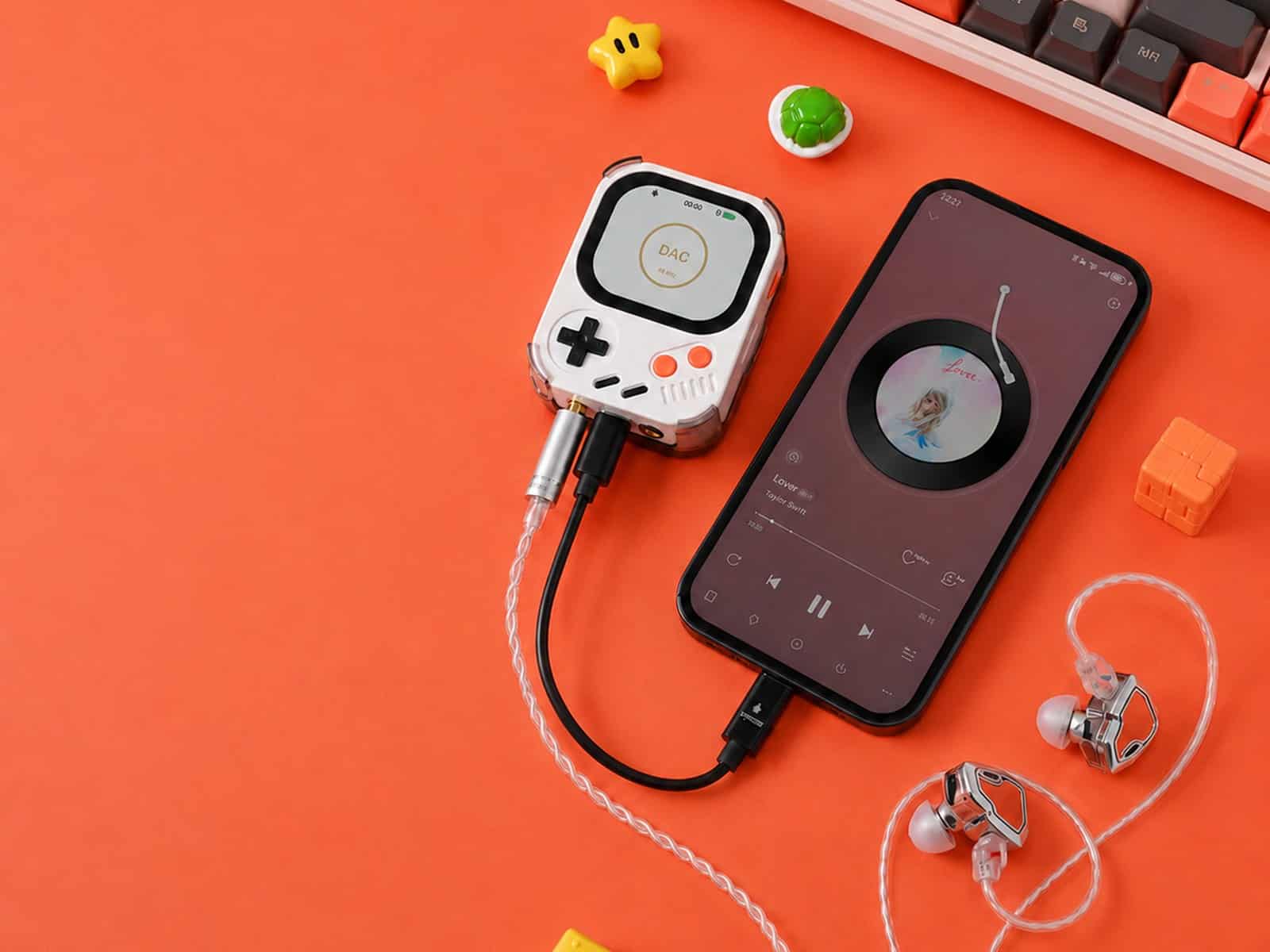 White Hidizs AP30 Music Boy connected by cable to a smartphone playing music, next to wired in-ear monitors and a mechanical keyboard
