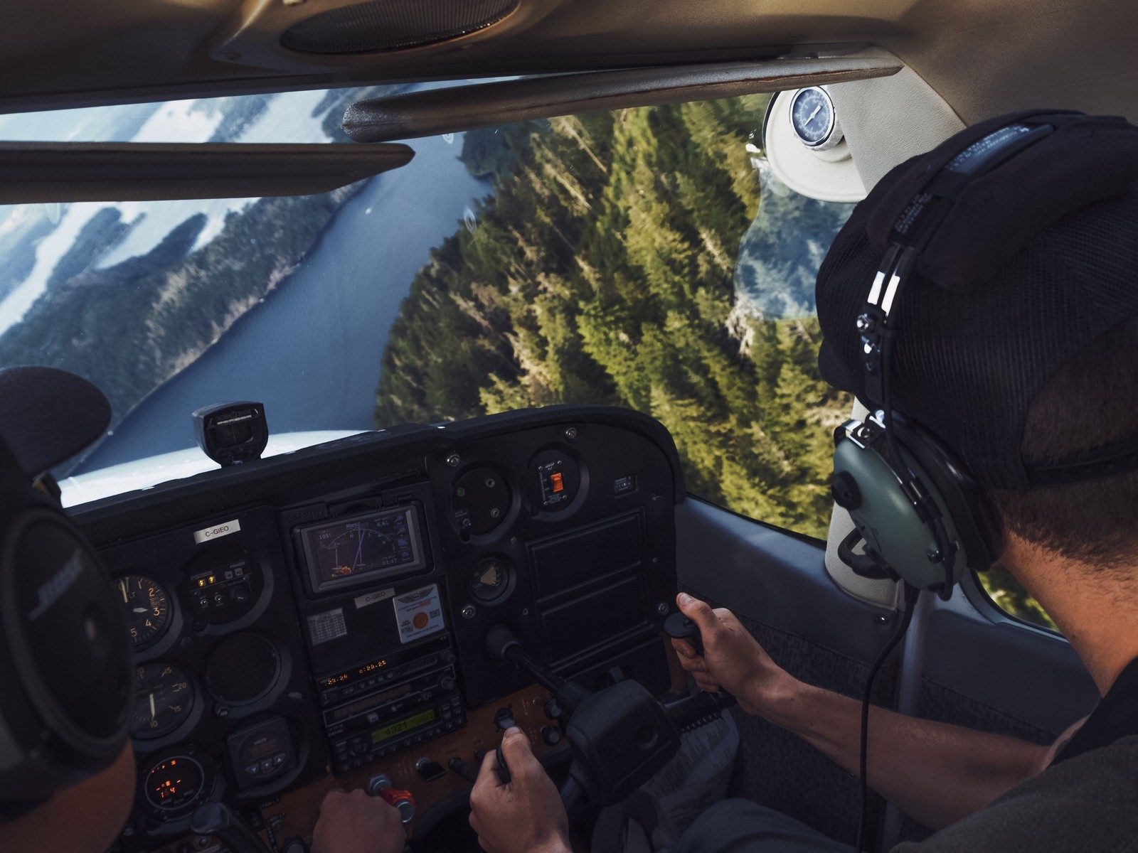 Two pilots at the controls of a light aircraft flying over a green river valley