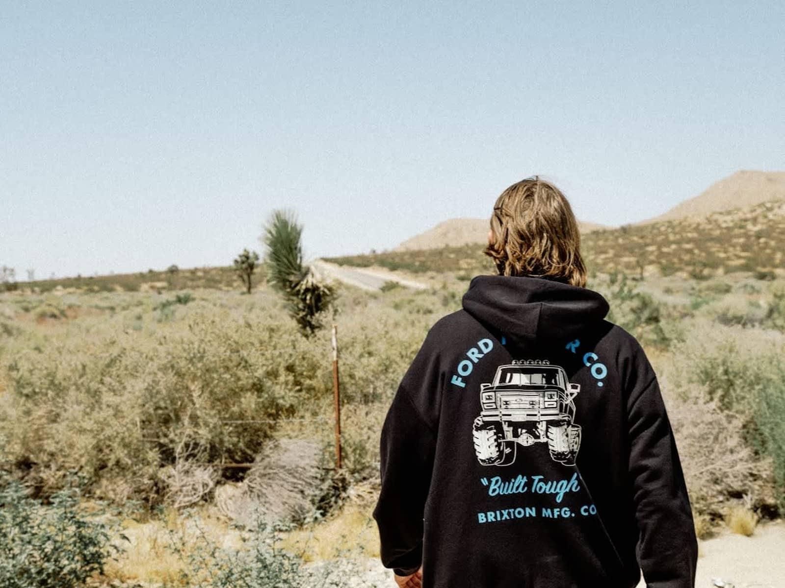 Model walking a desert road in the Ford Built Tough 4x4 Hood, monster truck back print in view