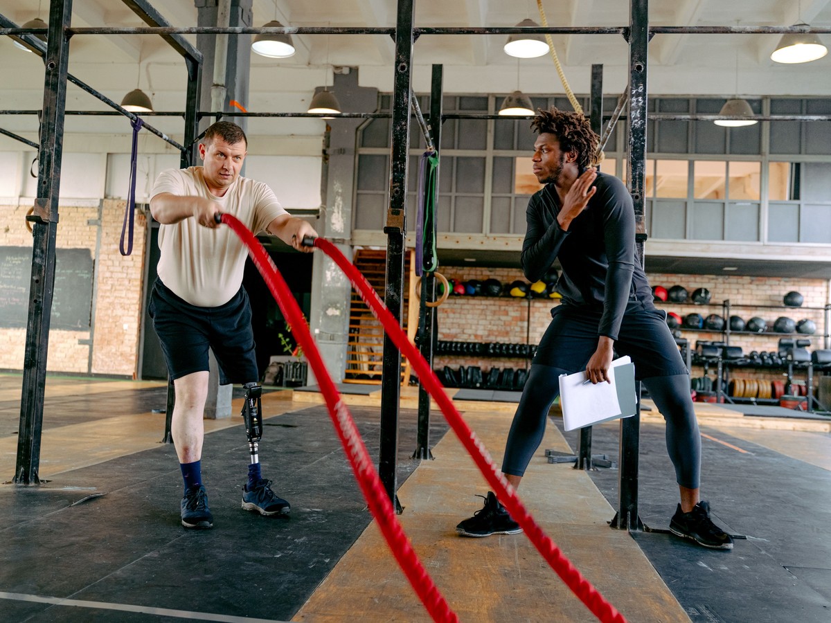 A personal trainer holding a clipboard while coaching a client through a battle ropes set